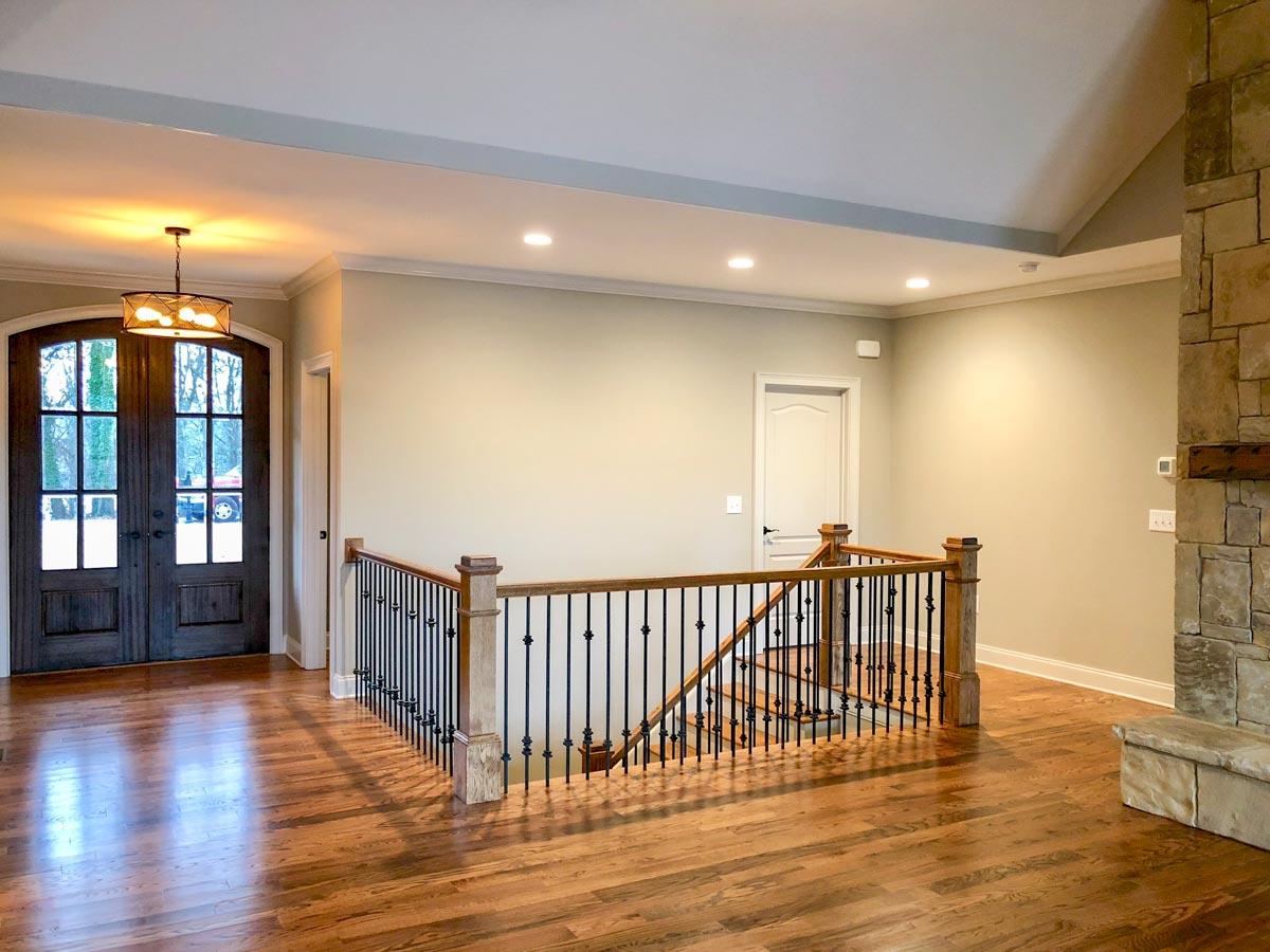 Interior view of house foyer with double wooden doors, staircase with black spindles, and stone fireplace.
