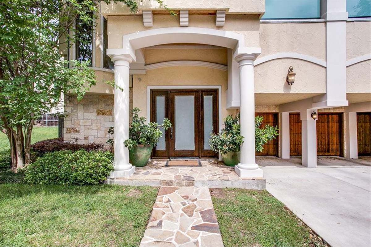House plan exterior with stone facade, arched portico, dual columns, and three garage bays.