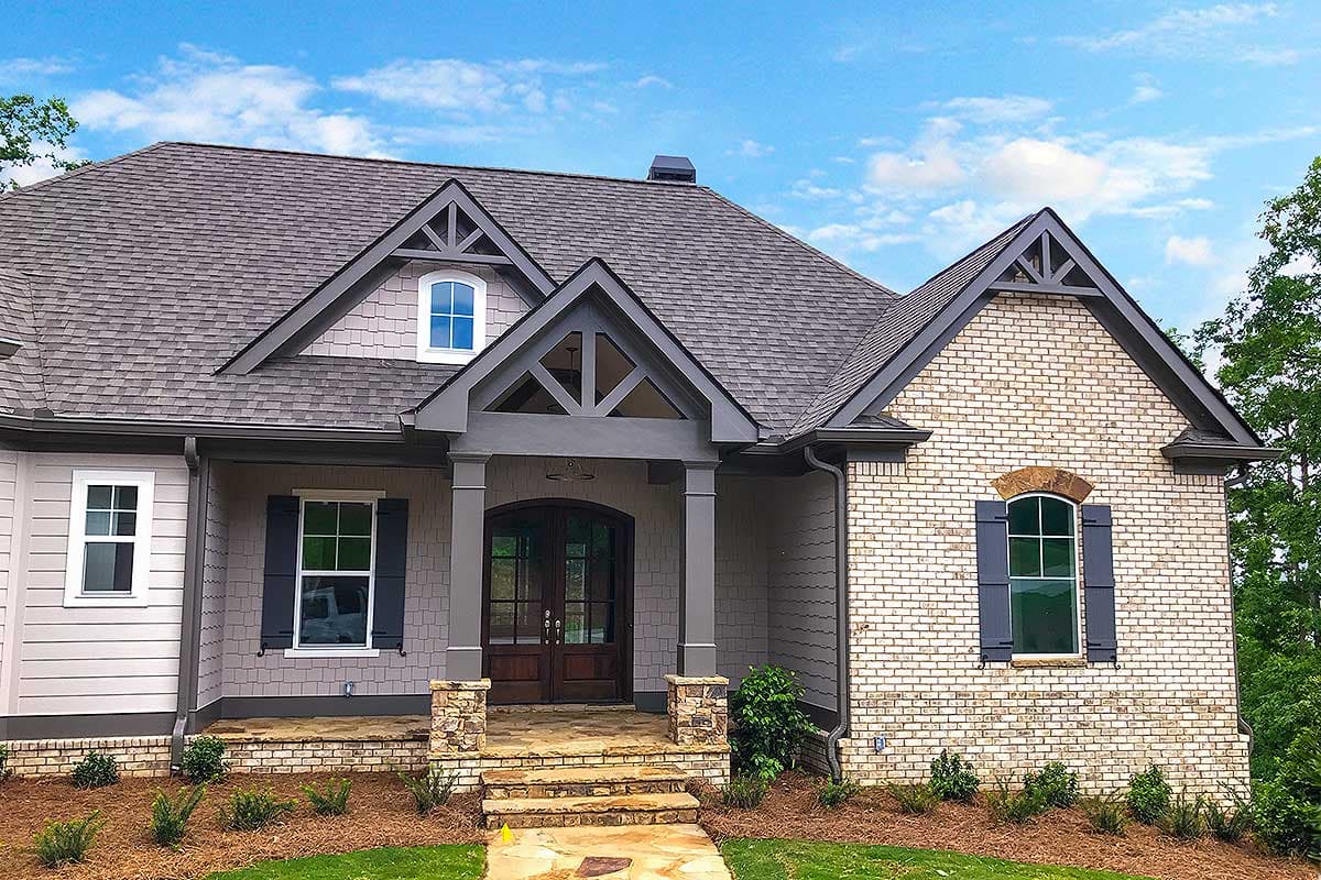 House plan exterior with gabled dormers, exposed rafter tails, stone-clad columns, and arched window.
