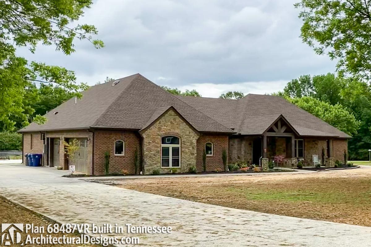 House plan exterior with brick and stone facade, gable rooflines, arched windows, covered porch, and attached garage.