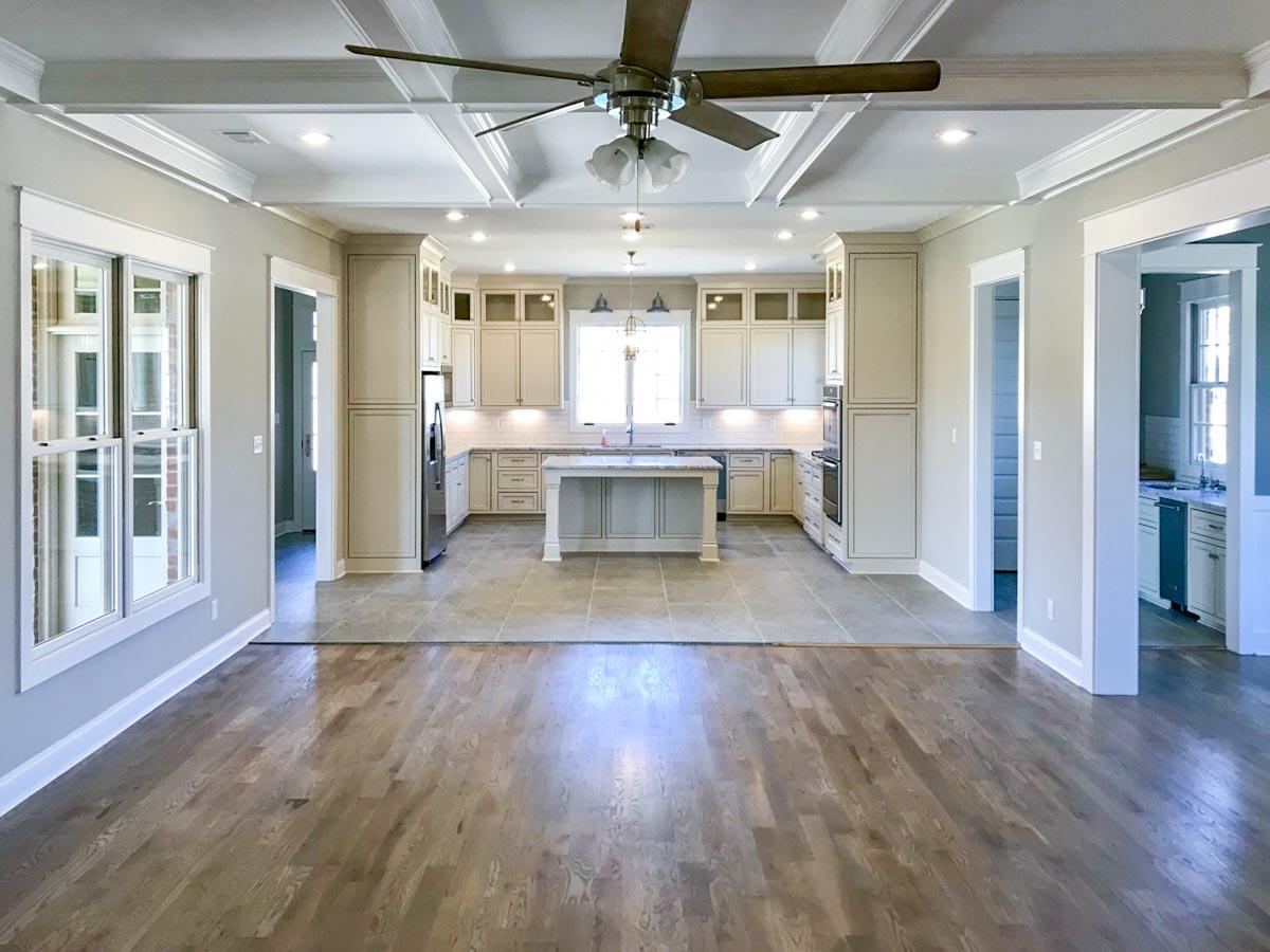 Interior view of an open-concept living space with a coffered ceiling, showcasing a kitchen with island and custom cabinetry, and a dining area.