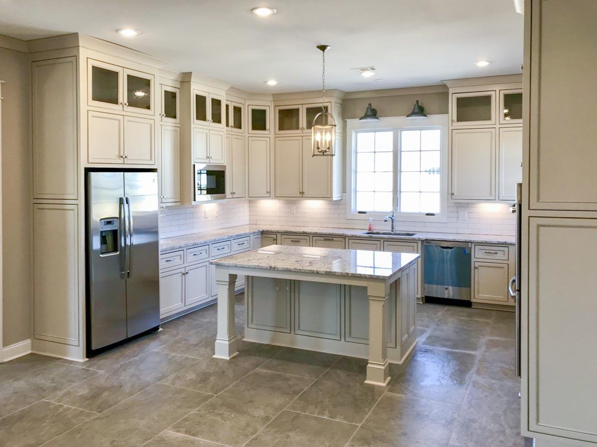 Kitchen with white cabinetry, granite island, stainless steel refrigerator, and subway tile backsplash.