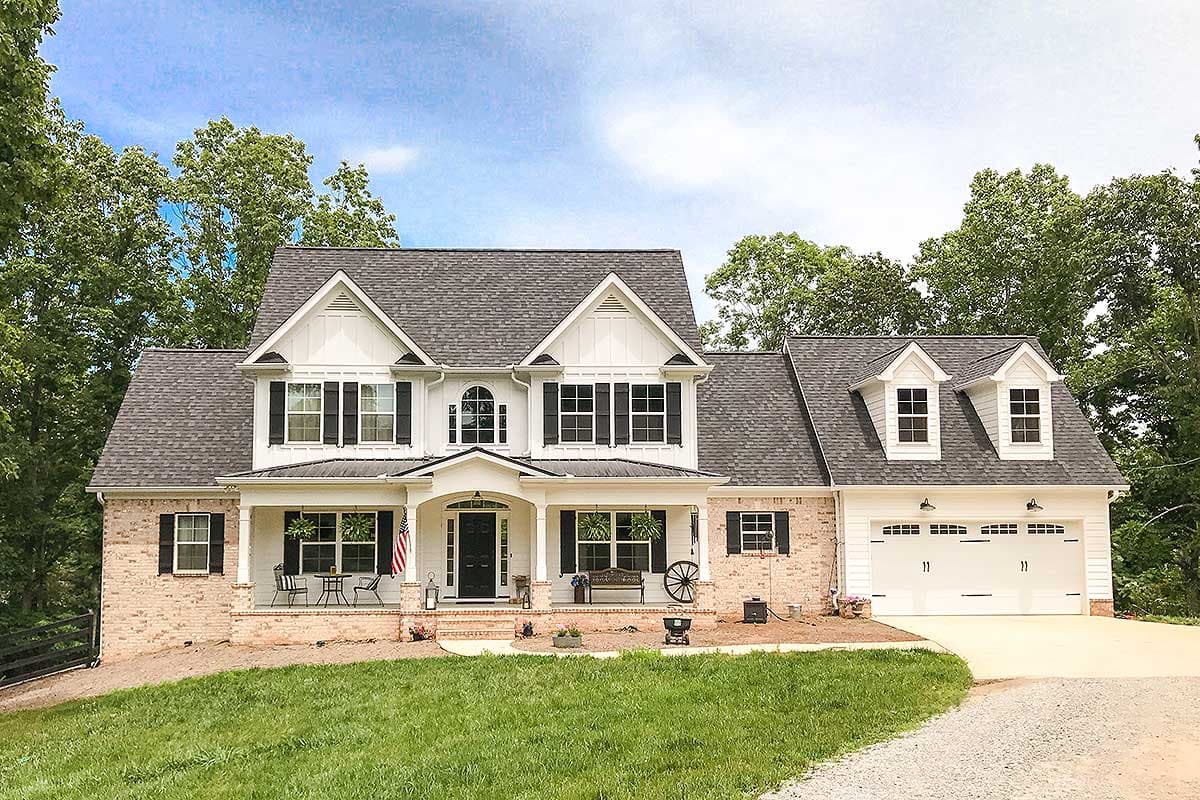 House plan exterior. Two-story farmhouse with front porch, gables, and garage with dormers. Brick and white siding exterior.