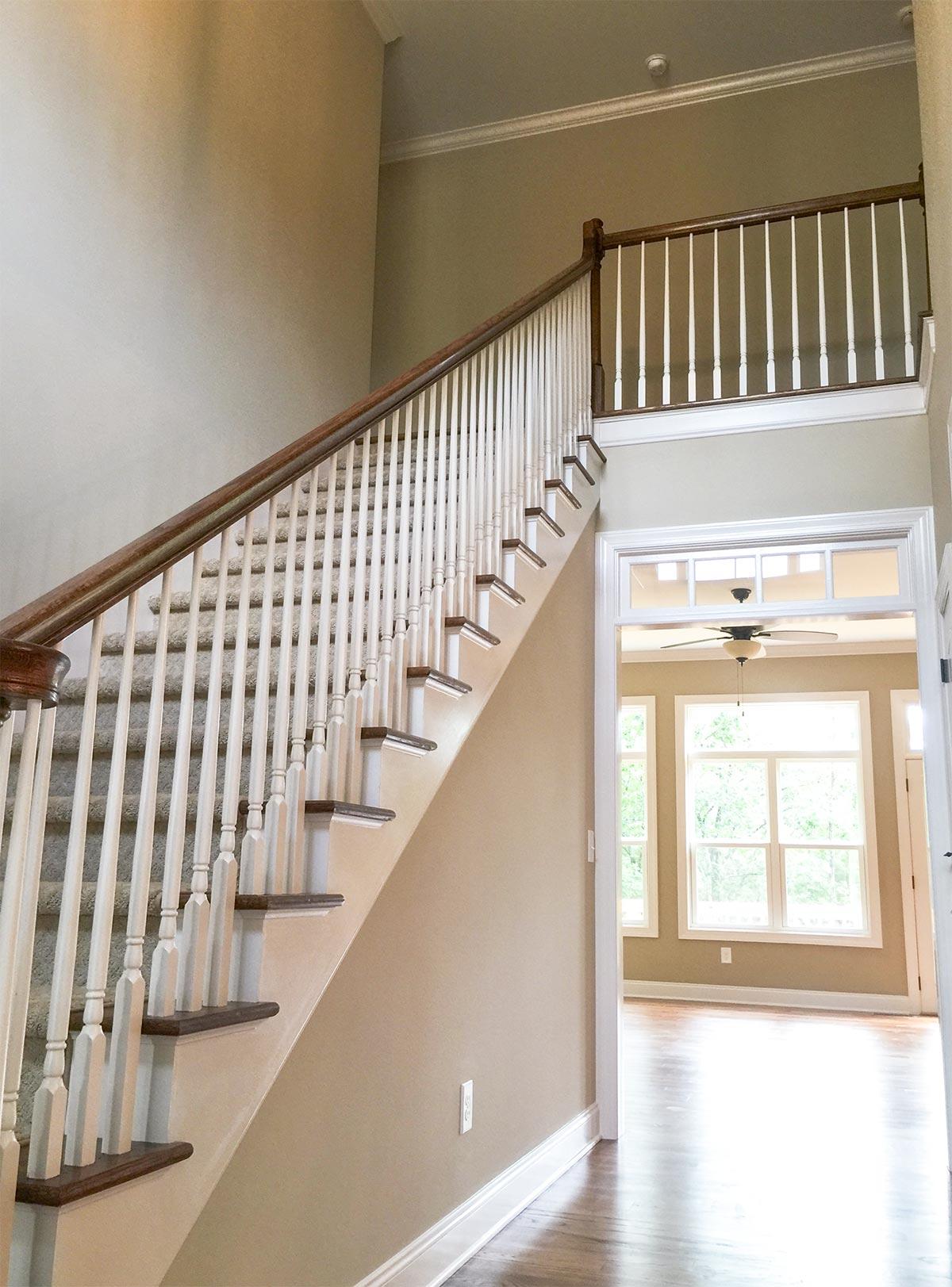 Interior view of a two-story foyer with a carpeted staircase featuring white balusters and a wooden handrail.