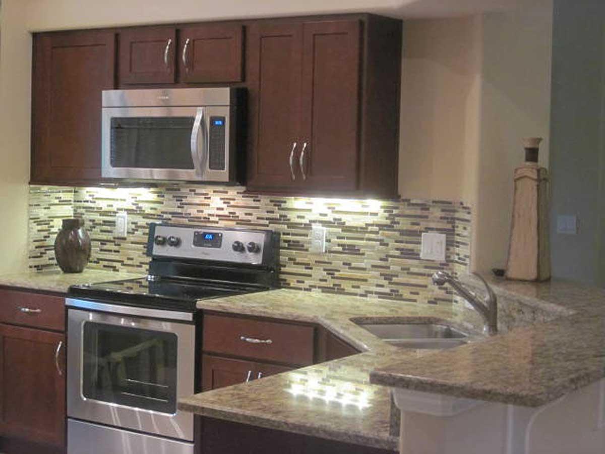 Kitchen with dark wood cabinets, granite countertops, stainless steel appliances, and mosaic tile backsplash.