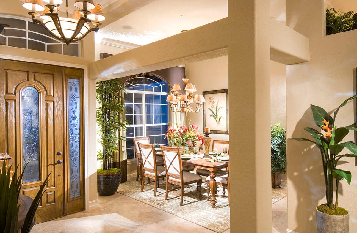 Dining room view from entryway, featuring a wooden table, chairs, chandelier, and large arched window.