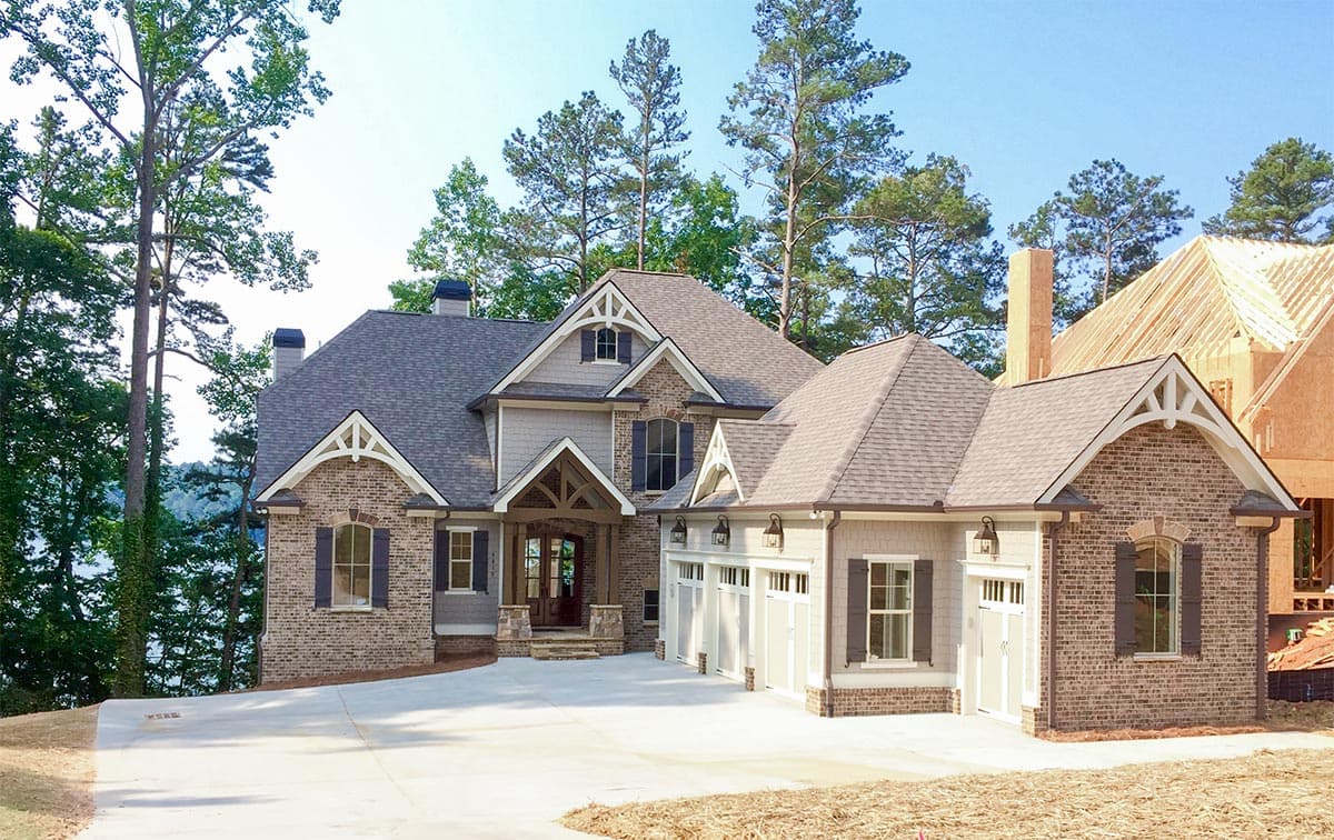 House plan exterior: Two-story home with brick and siding, multiple gables, covered entry, and a four-car garage.