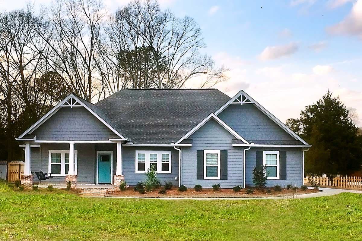 House plan exterior: Single-story home with covered front porch, gabled dormers, and horizontal siding.