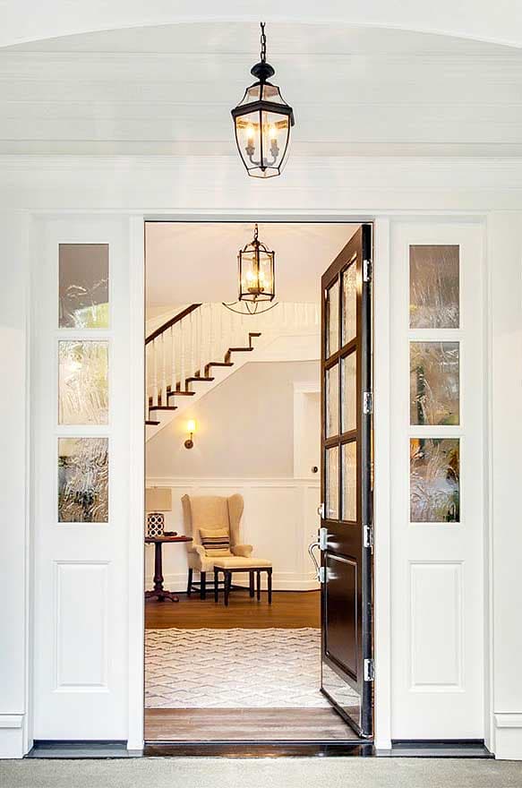 Entrance hall with open door, staircase, armchair, and decorative pendant lighting.