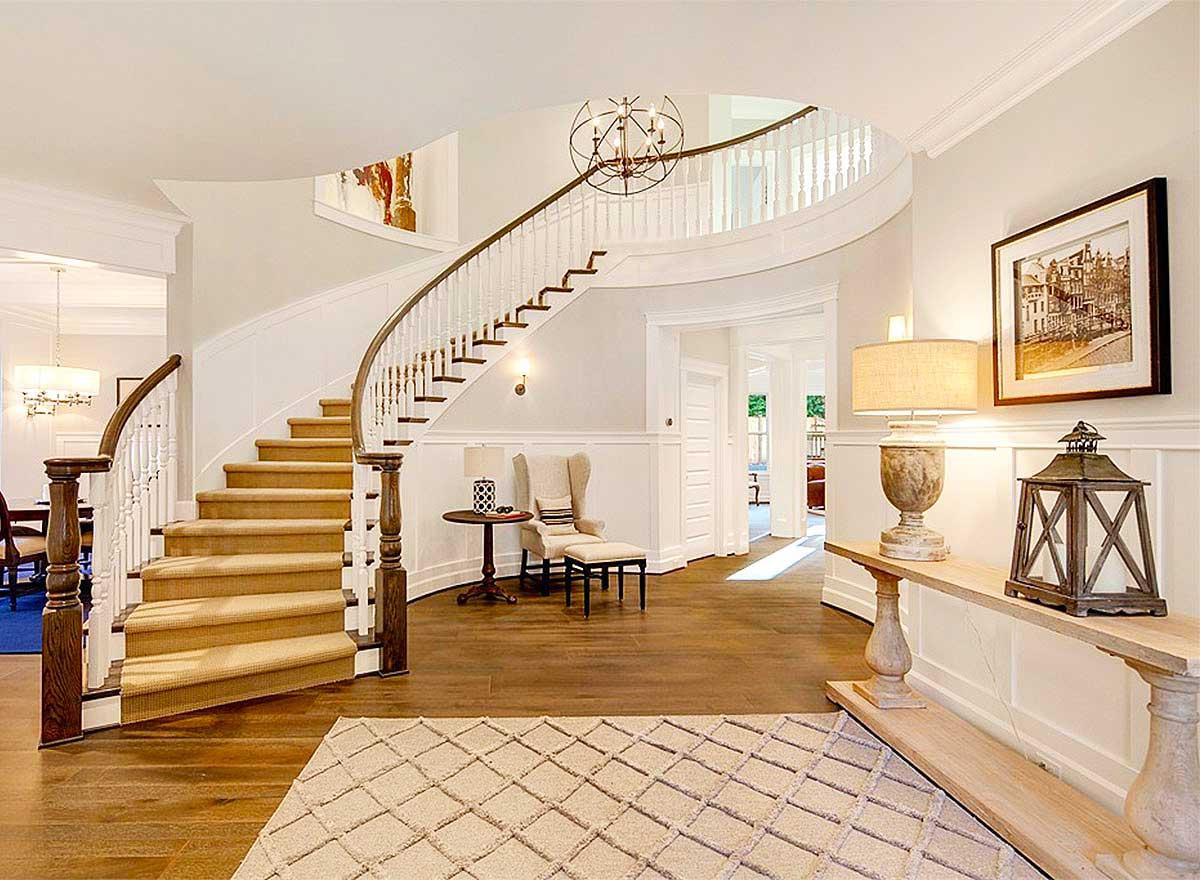 Interior view of a grand foyer with a curved staircase, wainscoting, and a central chandelier.