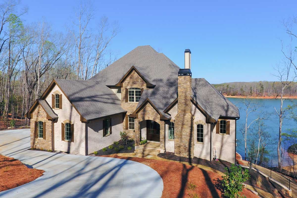 House plan exterior shows a two-story home with stone accents, prominent chimney, multiple gables, and arched entryway.