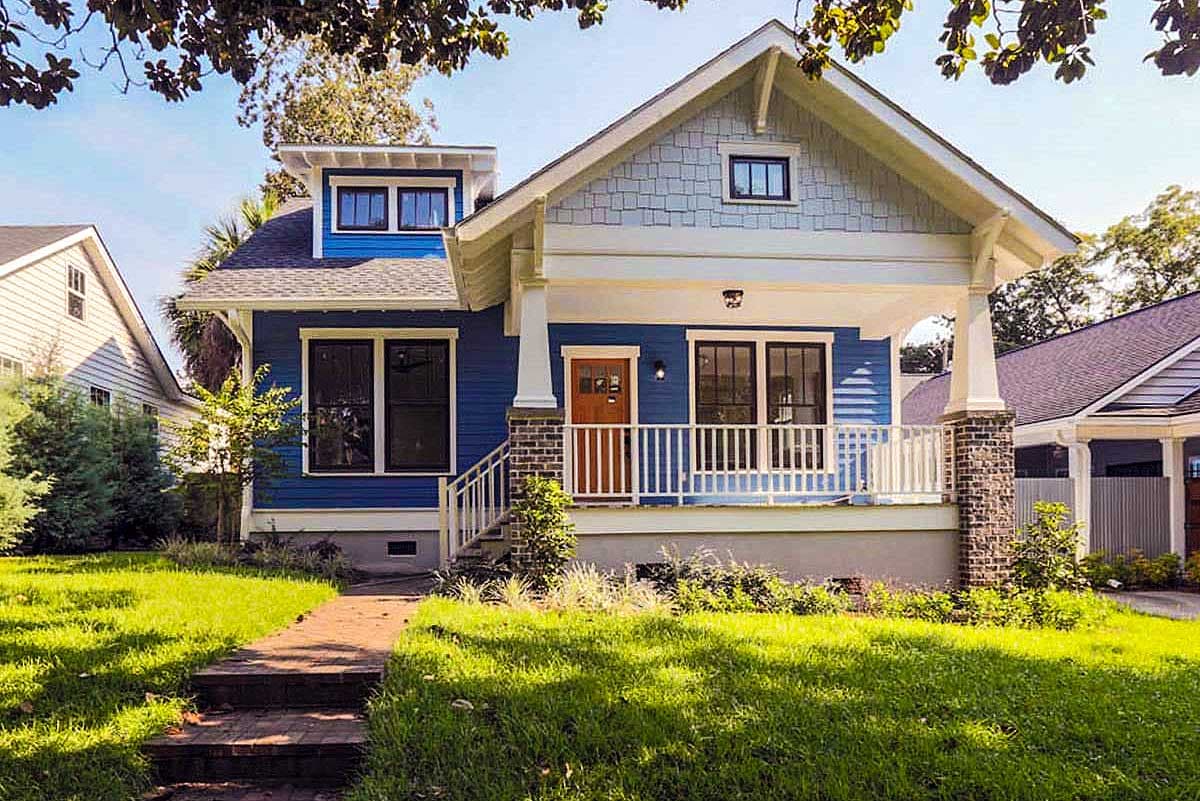 Craftsman-style house plan exterior with a single story, gabled roof, front porch with columns, and a dormer. Features blue siding and brick accents.