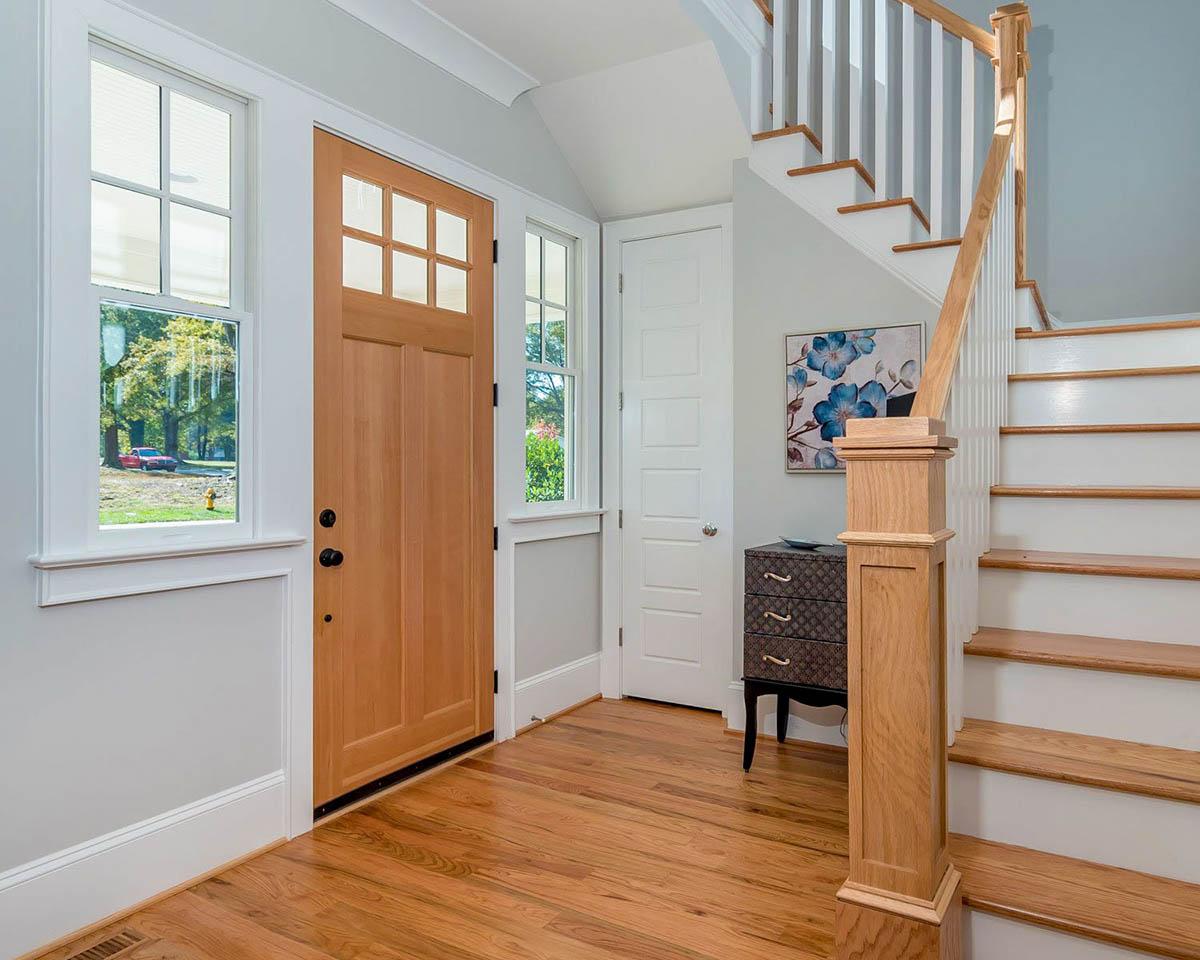Interior view of home entryway with wood door, windows, and staircase. Includes decorative chest and artwork.