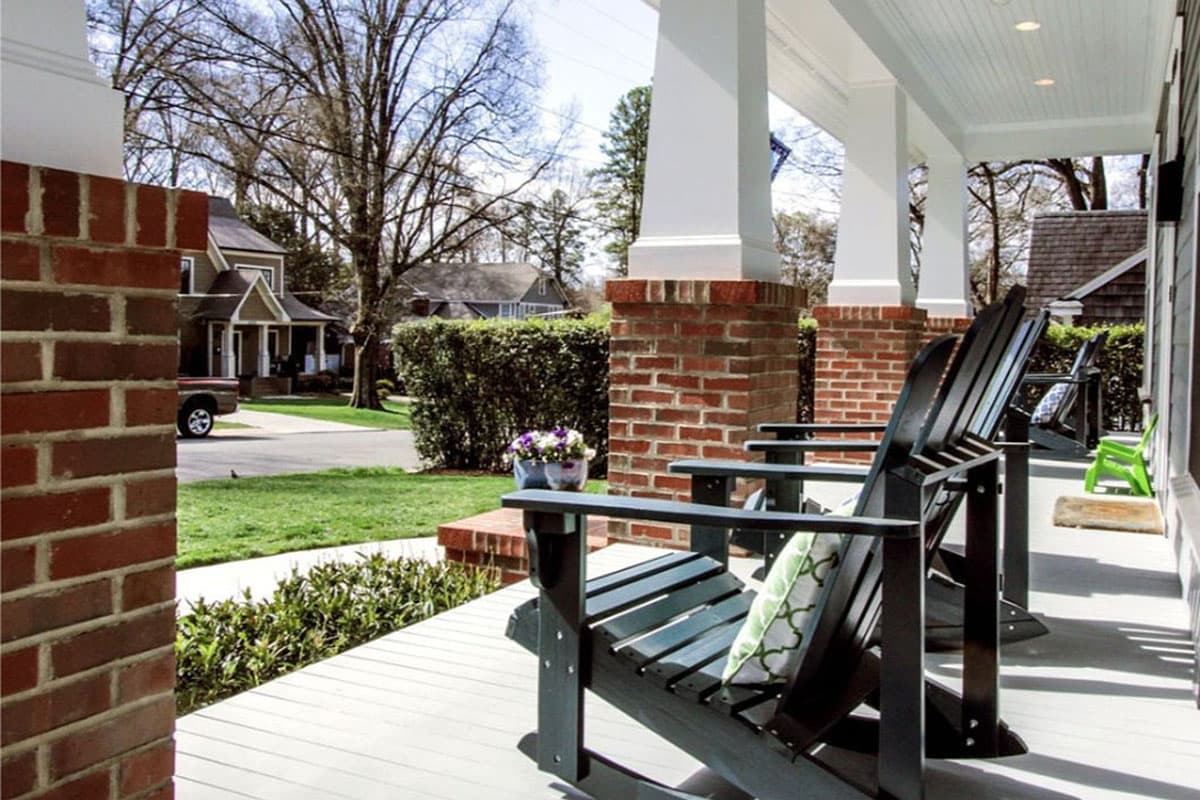 Front porch exterior with brick pillars, white columns, and Adirondack chairs.