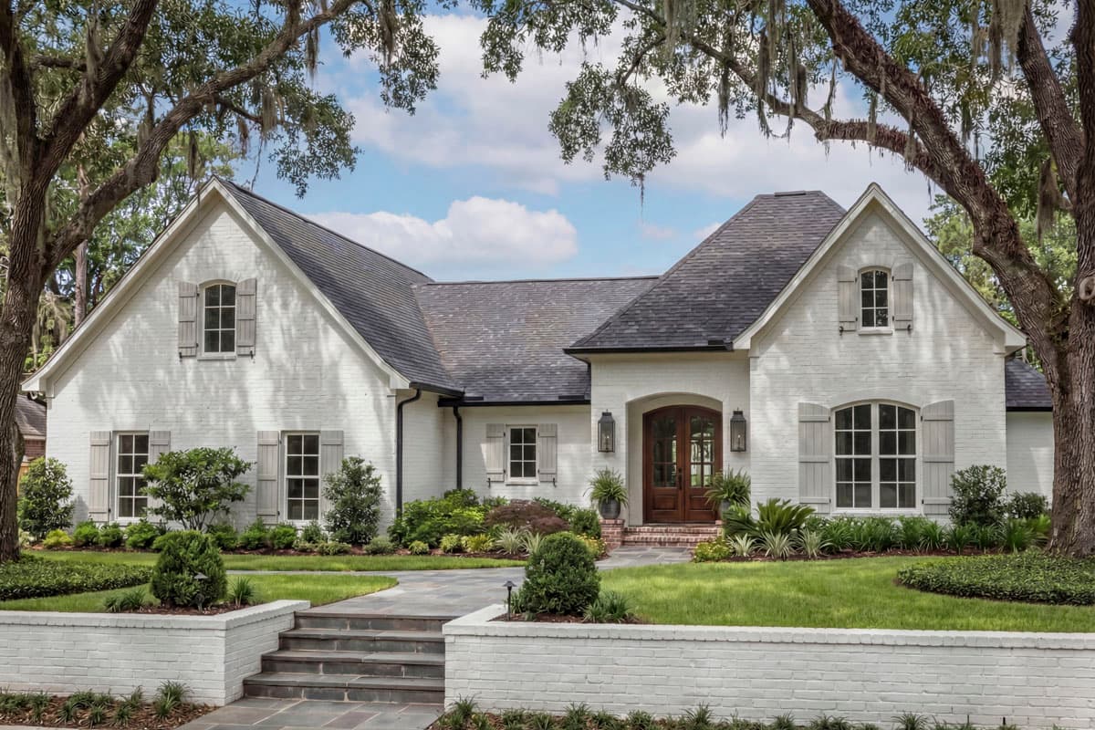 Exterior house plan: white brick, two stories, gabled rooflines, arched double front doors, and louvered shutters.
