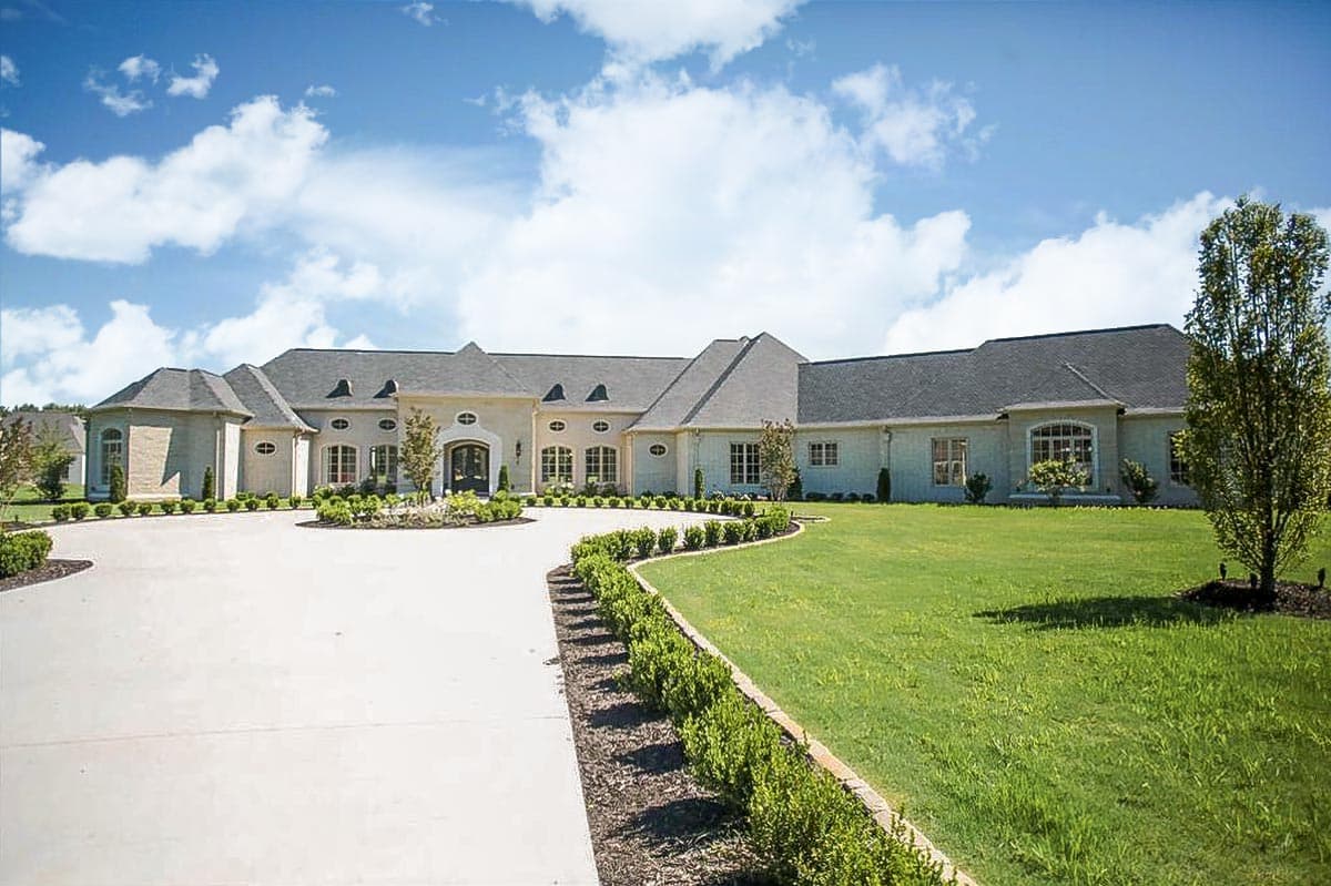 House plan exterior: sprawling one-story home with mansard rooflines, arched windows, and a circular driveway.