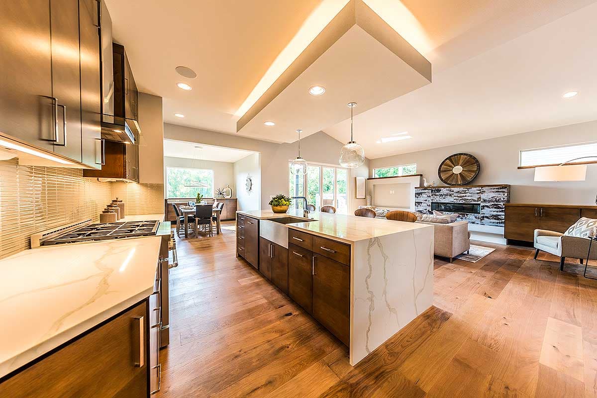 Open concept living area featuring a kitchen island with waterfall countertop, gas range, fireplace, and dining area.