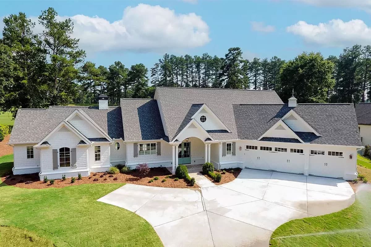 House plan exterior view, featuring a white, one-story home with a gabled roof, dormers, and a garage with multiple bays.