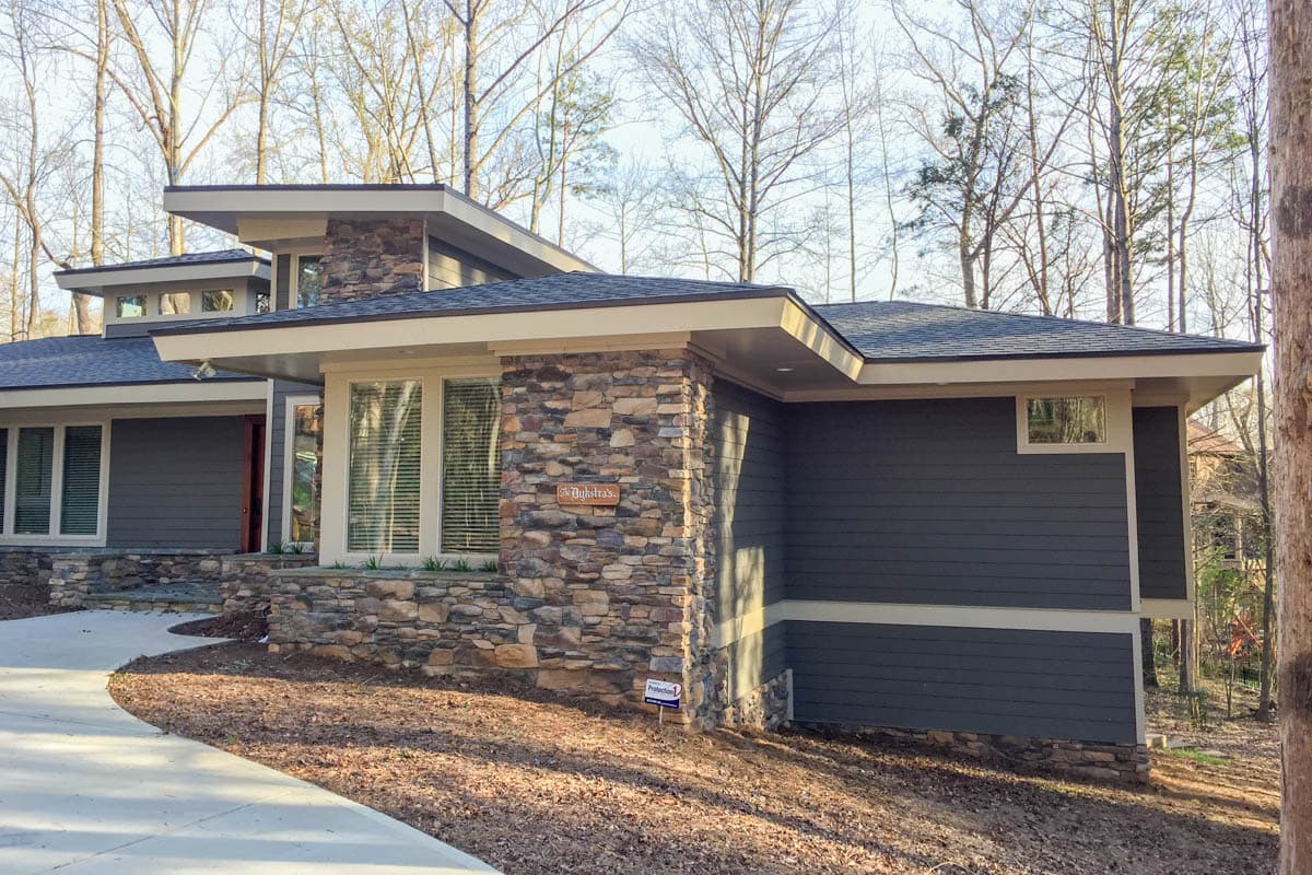 Modern house plan exterior with stacked stone accents, layered rooflines, and dark horizontal siding.