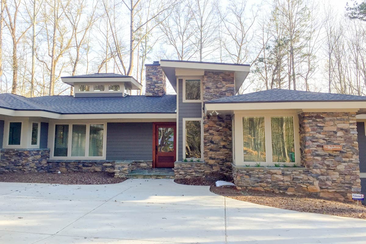 Modern house plan exterior with stone accents, multiple gables, clerestory windows, and a central wood door.