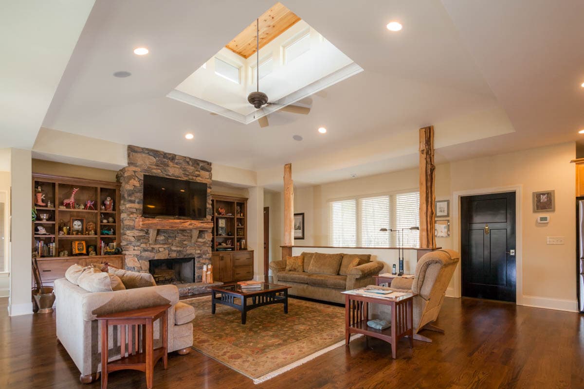 Living room with stone fireplace, built-in bookshelves, skylight with fan, and wood flooring.