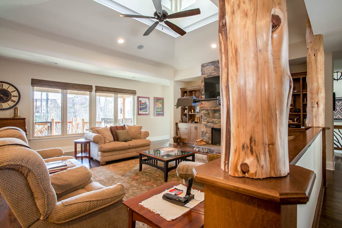 Living room with vaulted ceiling, skylight, stone fireplace, and exposed log structural supports.