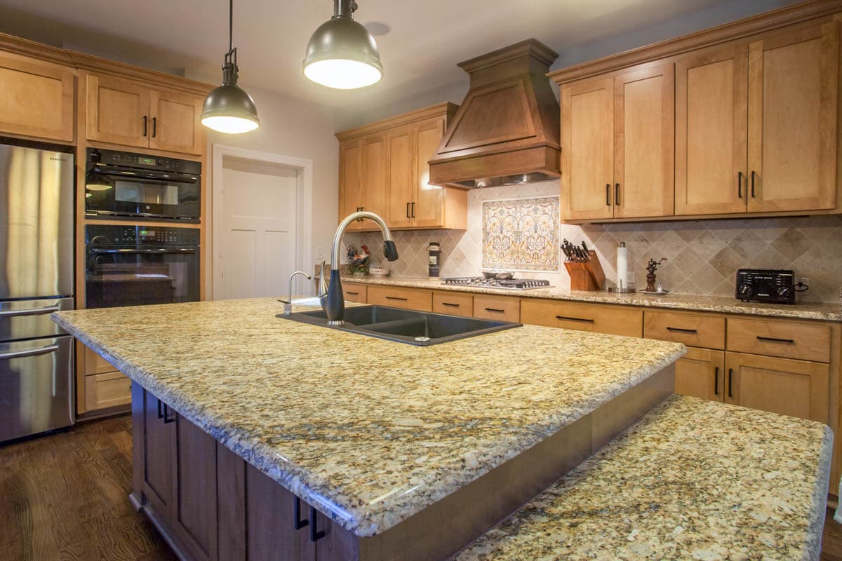 Kitchen with large granite island, double ovens, stainless steel refrigerator, and wood cabinetry.