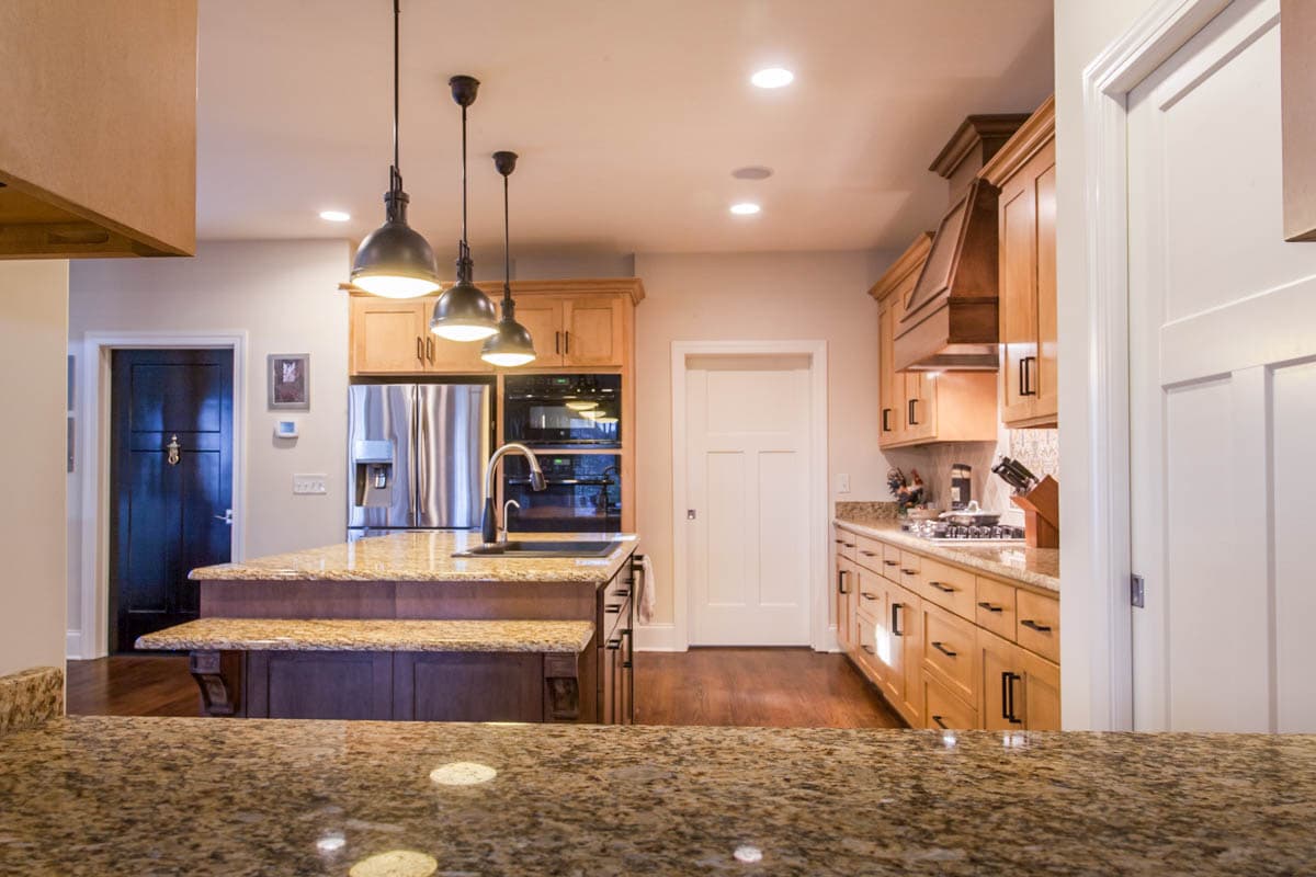 Kitchen interior with island, stainless steel appliances, wood cabinetry, granite countertops, and pendant lighting.