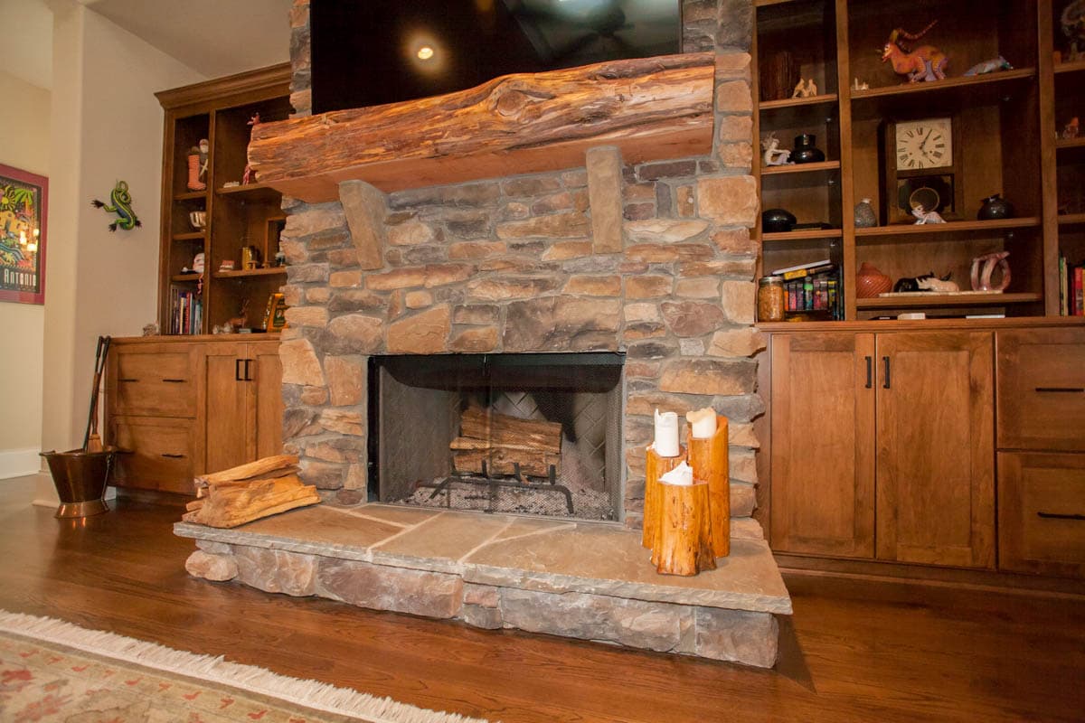 Stone fireplace with rustic log mantel and built-in wooden cabinetry and shelving.