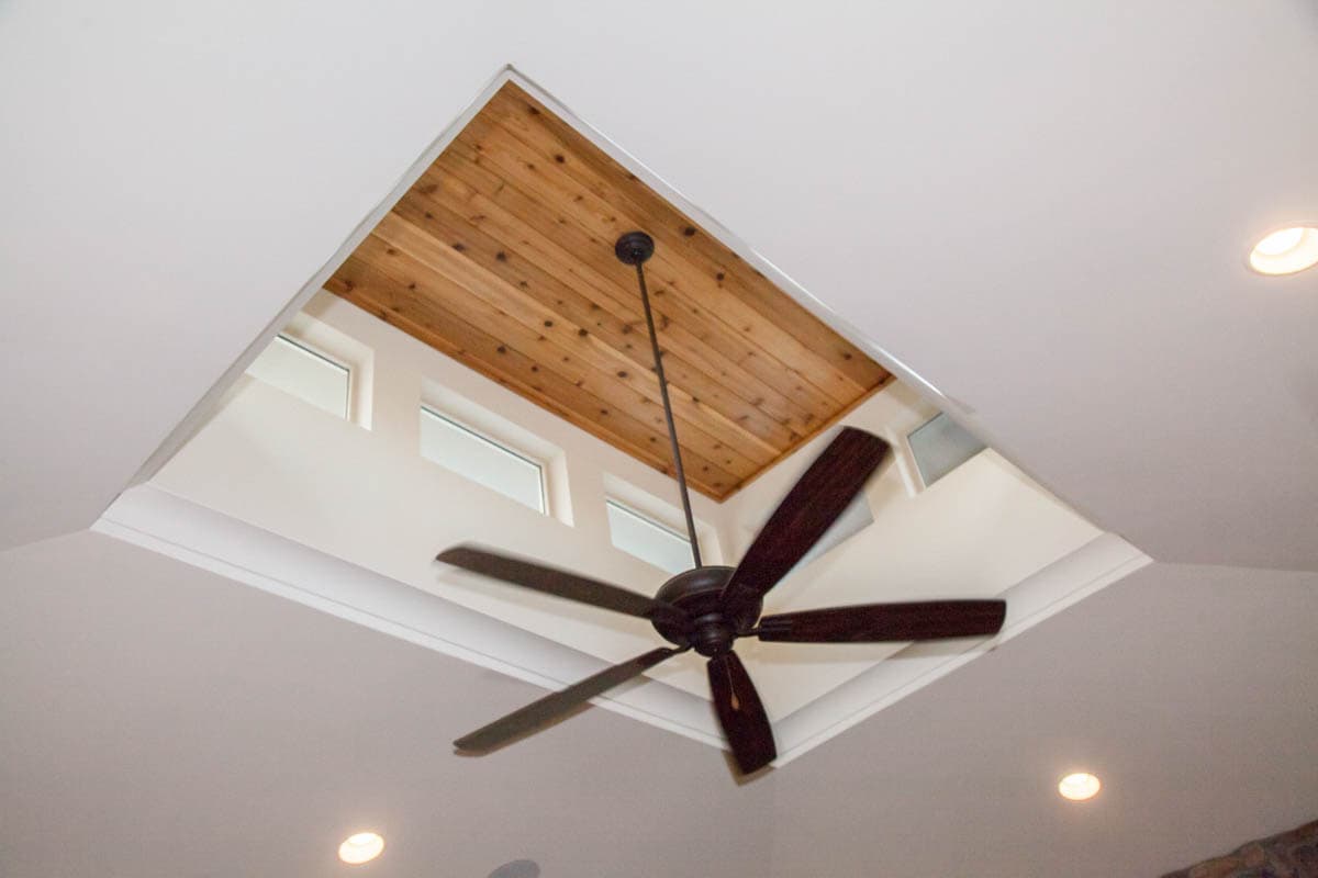 Interior view of a vaulted ceiling with a wood-paneled accent, central ceiling fan, and clerestory windows.