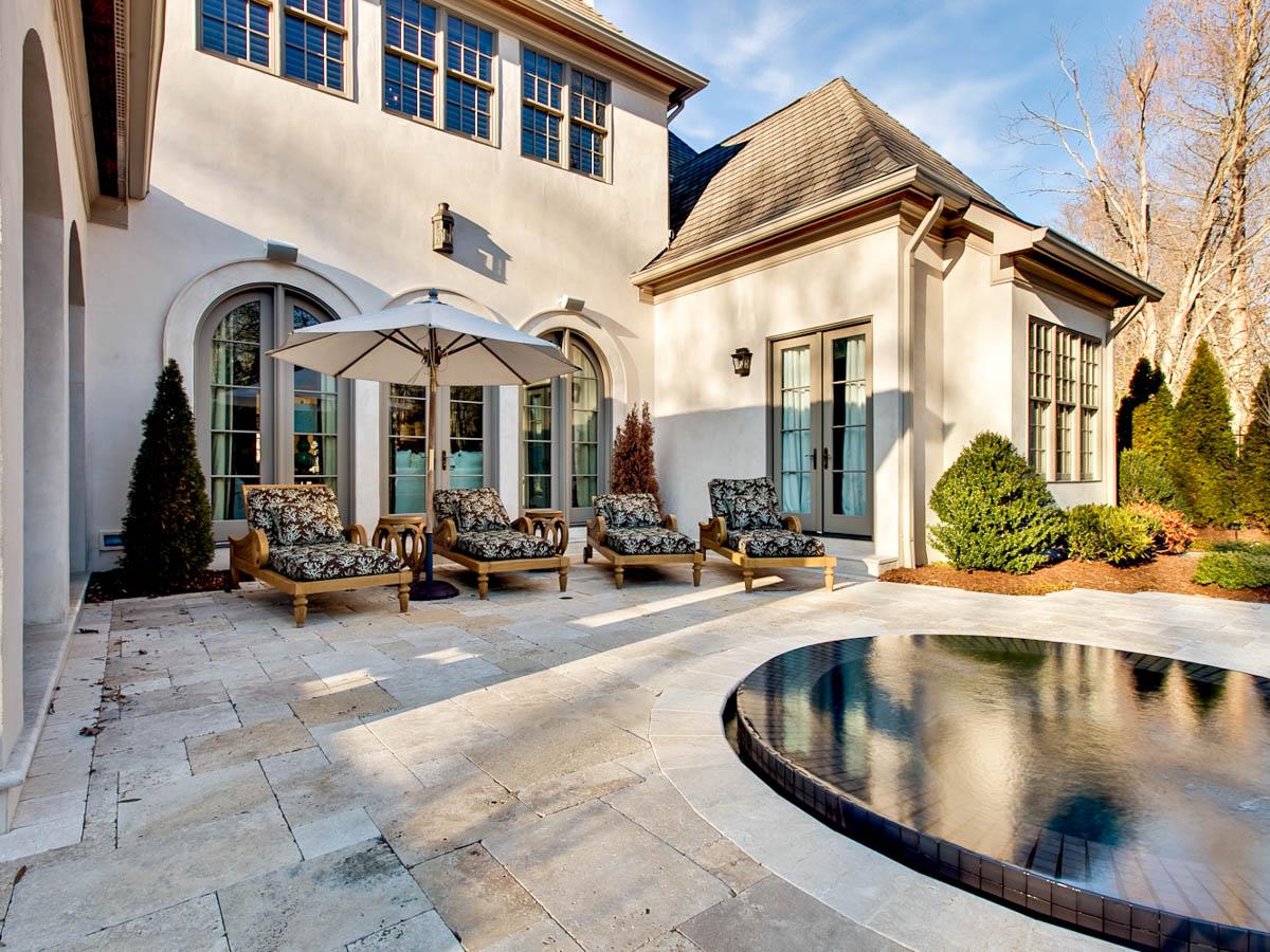 House plan exterior view of a large home with arched windows, chaise lounges, an umbrella, and a circular pool.