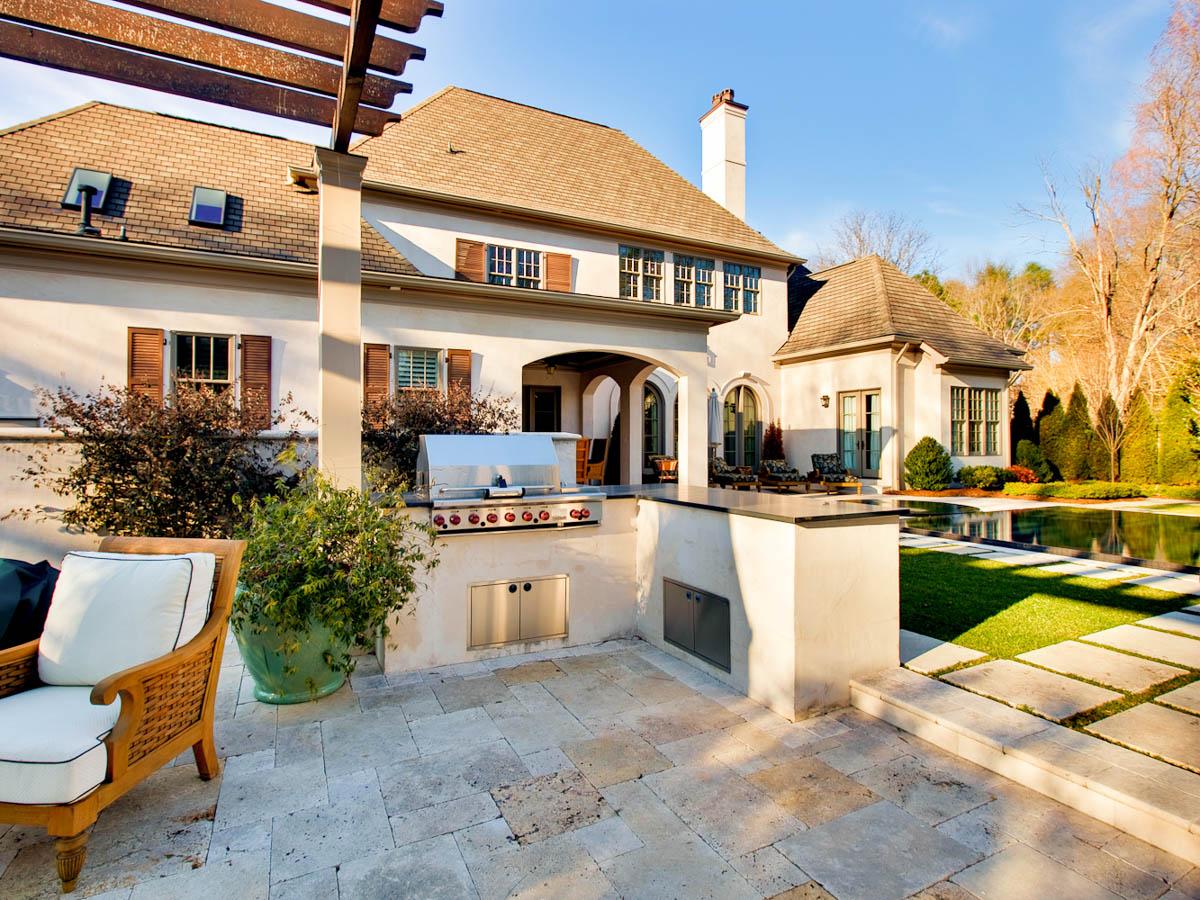 House plan exterior: Two-story home with stucco finish, arched entryway, covered patio, built-in grill, and pergola.