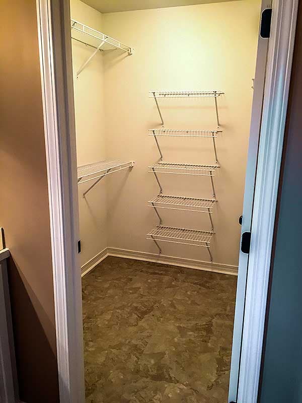 Empty walk-in closet with wire shelving on two walls and marble-patterned flooring.