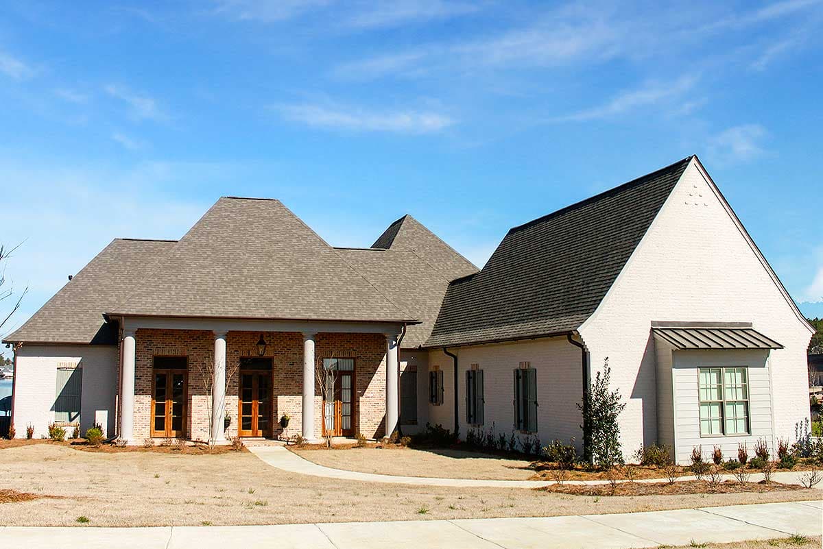 House plan exterior. One-story home with multiple rooflines and gables. Features include a covered porch with columns and shuttered windows.