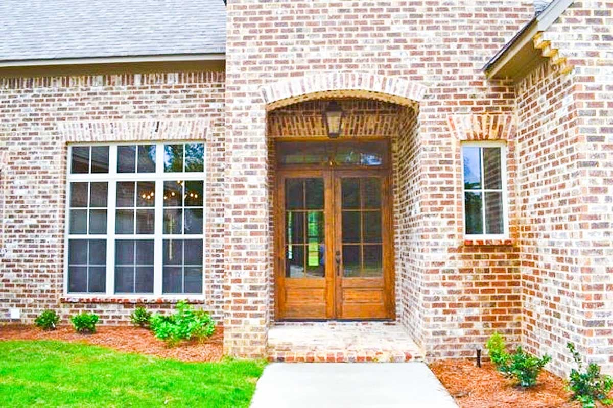 House plan exterior with brick facade, arched entryway with double wooden doors, and multi-pane windows.