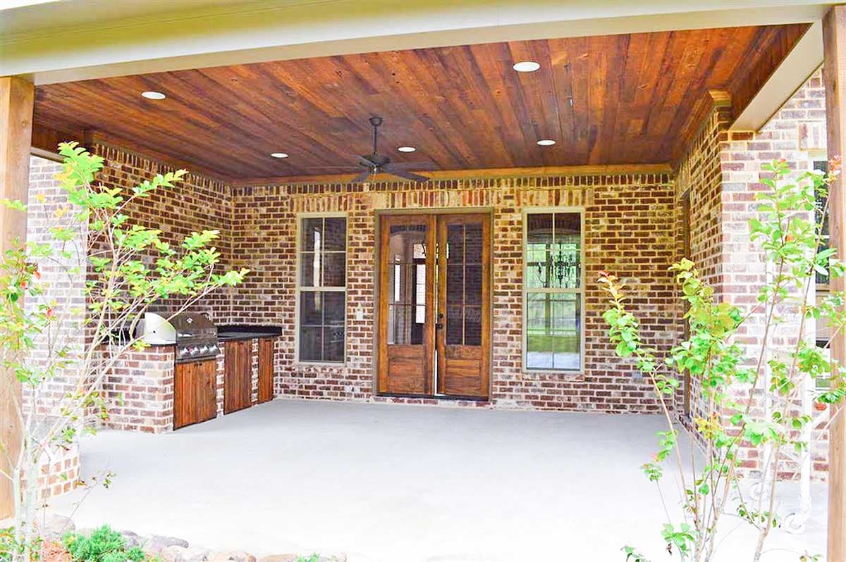 Exterior view: covered patio with brick walls, wood ceiling, outdoor grill station, and double glass doors.