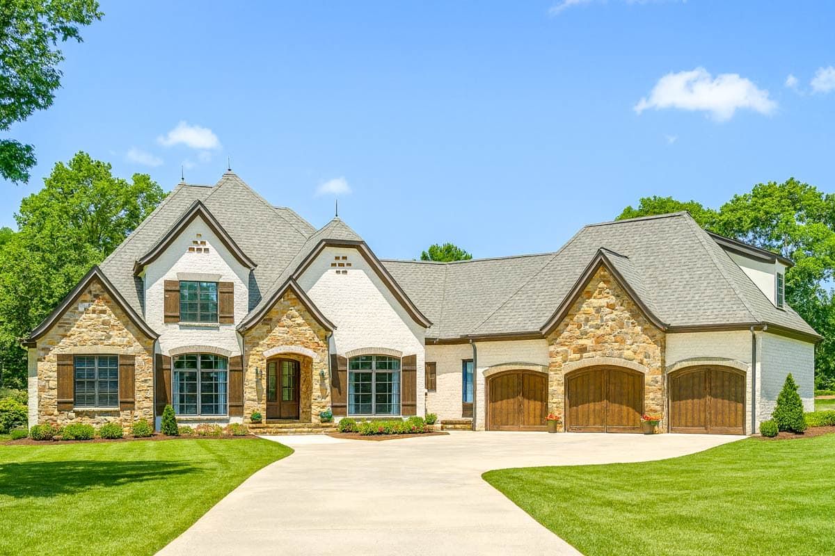 House plan exterior with stone accents, multiple gables, and arched garage doors. Features a two-story design and a curved driveway.