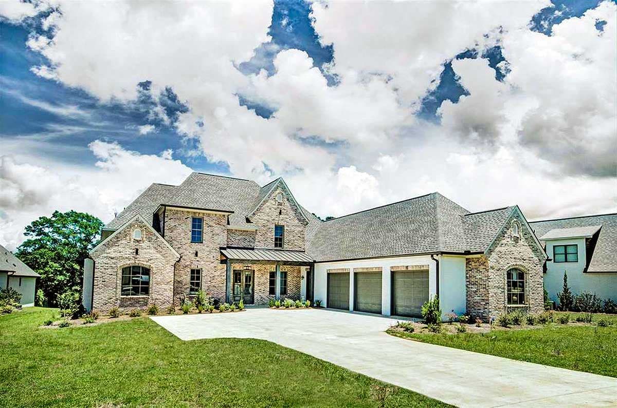 House plan exterior. Two-story brick home with gabled rooflines, arched windows, and a three-car garage. Features a covered front porch.