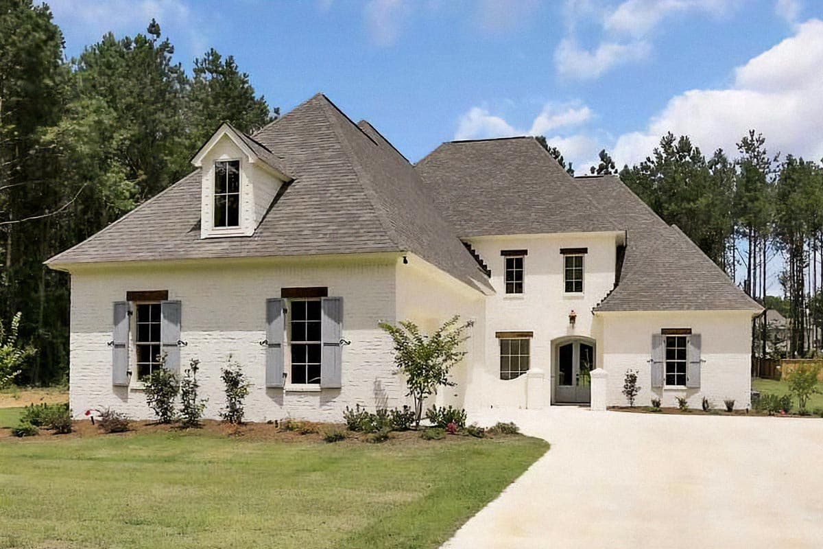 House plan exterior featuring a two-story design with gabled rooflines, dormers, and multiple windows with shutters. Brick facade and light driveway.