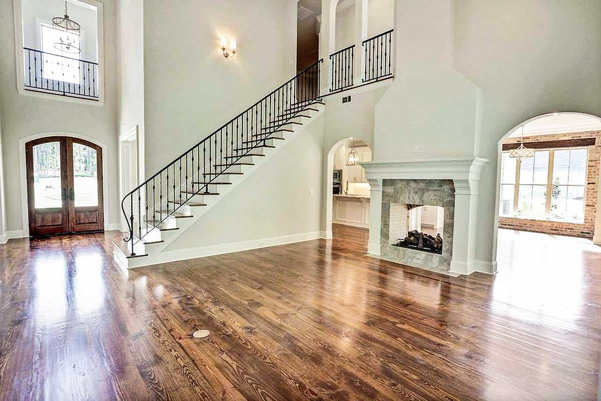 Great room interior with stone fireplace, grand staircase, double entry doors, and open archway to kitchen.