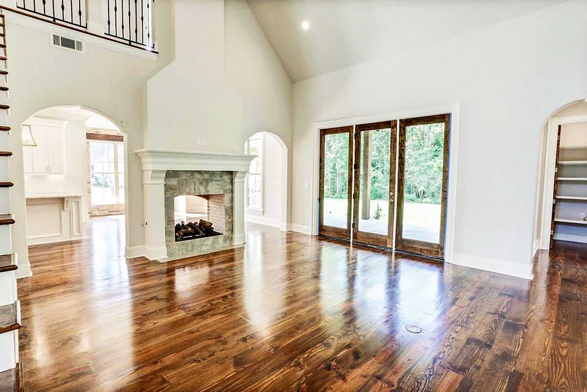 Great room with vaulted ceiling, stone fireplace, arched entry to kitchen, and glass doors.
