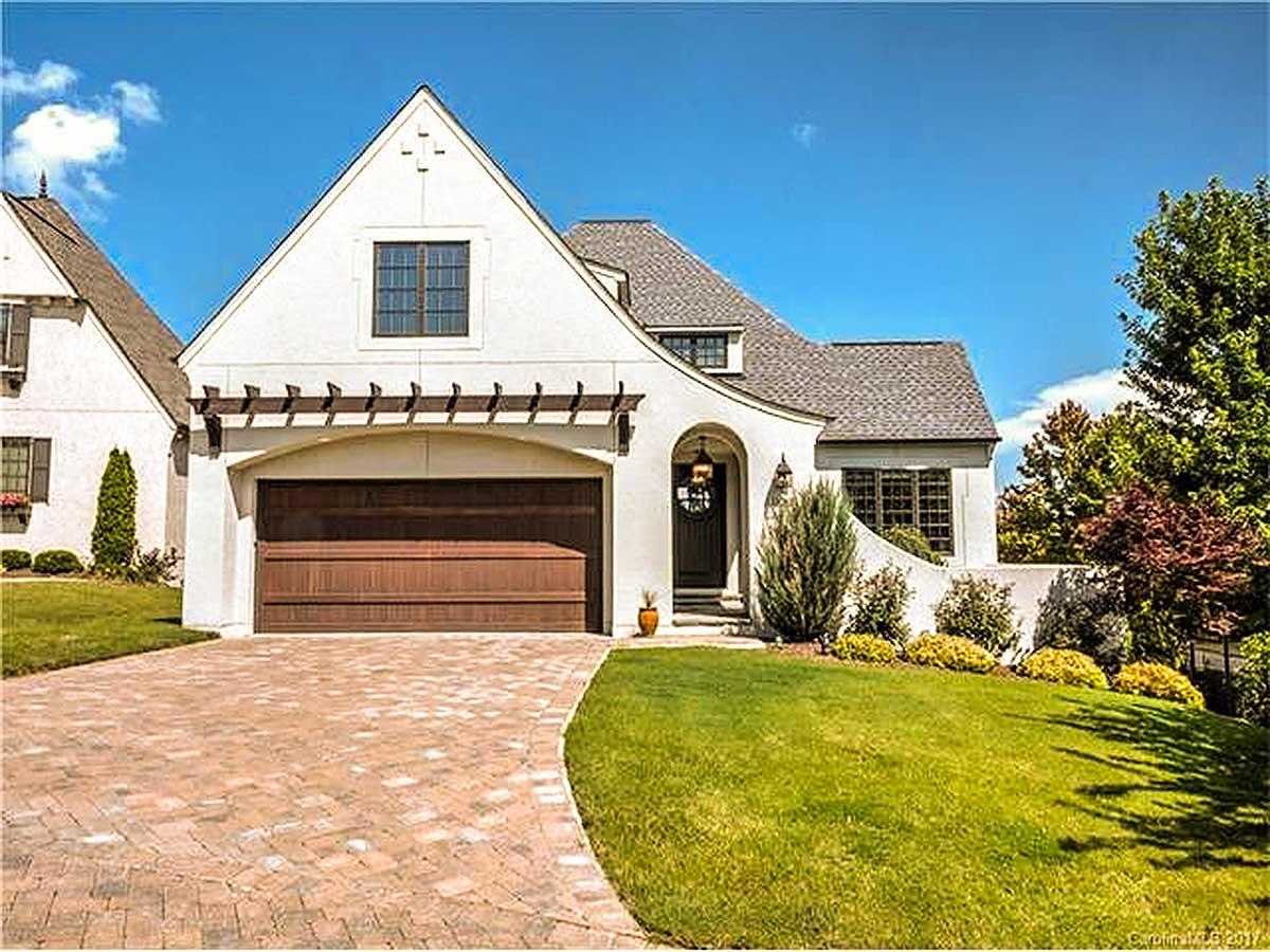 European-inspired house plan exterior with stucco finish, arched entryway, gable dormer, and attached garage with pergola.