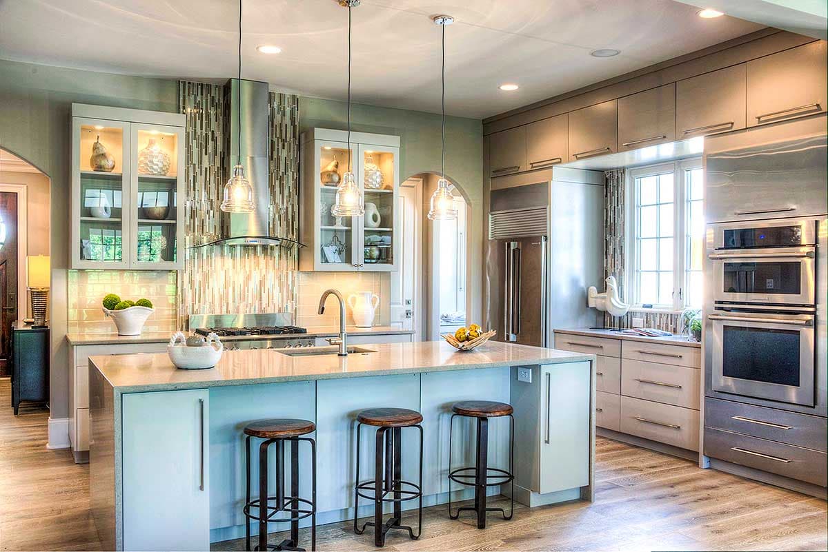 Contemporary kitchen with island, stainless steel appliances including double ovens and refrigerator, and glass-front cabinets.