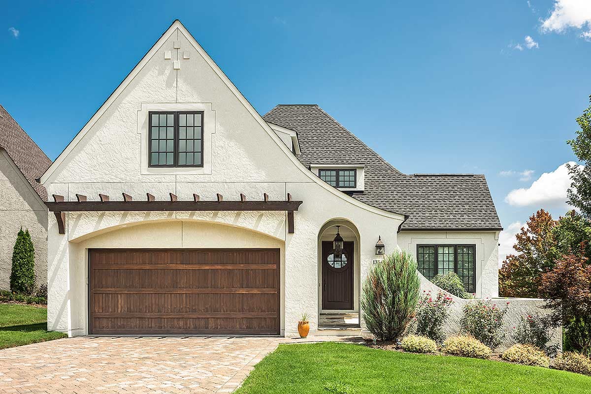 House plan exterior featuring a two-story design with a stucco facade, eyebrow roof, dormer, arched entry, and detached garage.