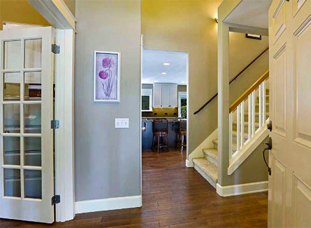Interior view of a house entry with glass-paneled doors, view of a kitchen with island, and a staircase with white balusters.