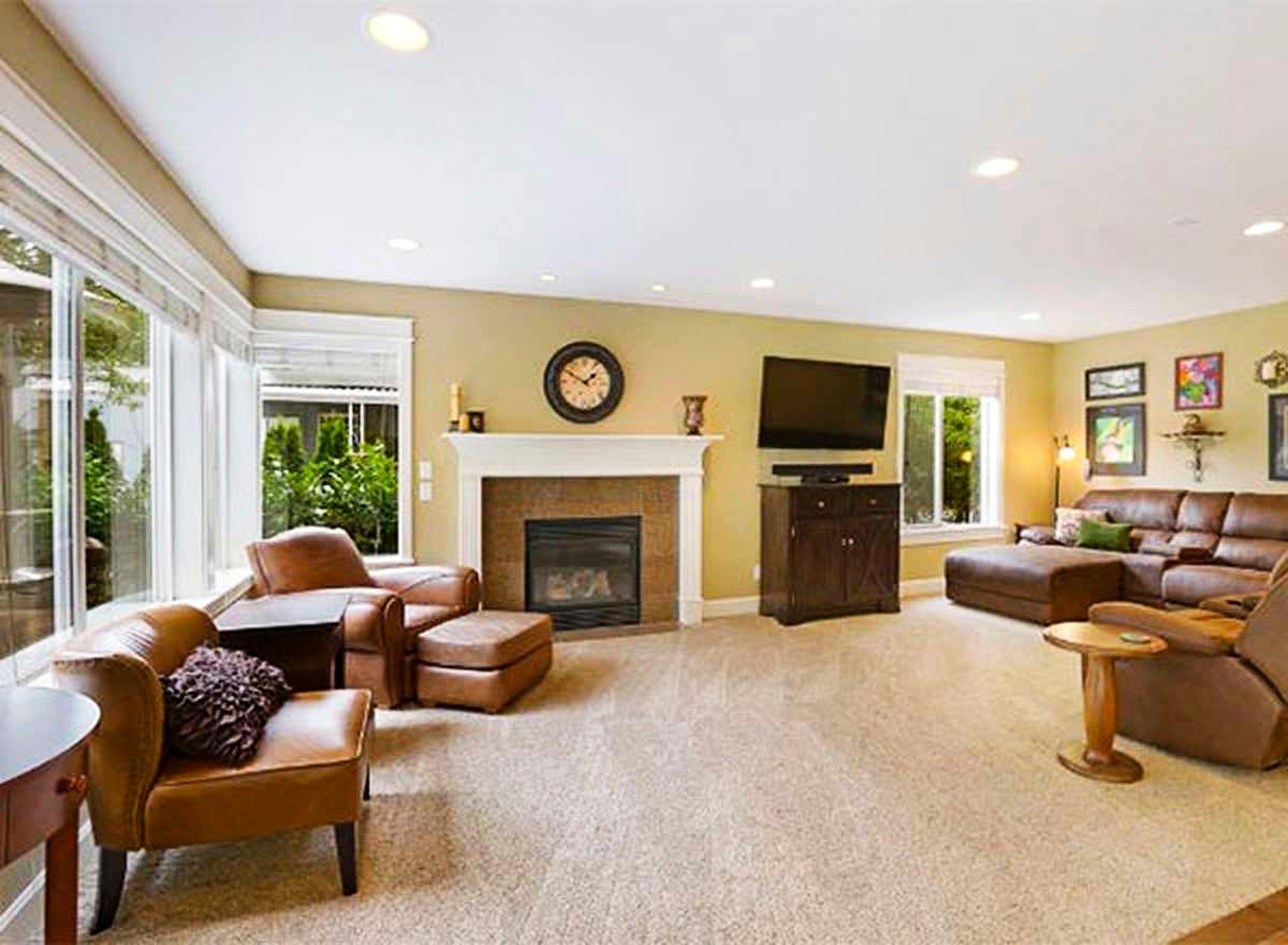 Great room with fireplace, sectional sofa, media console, and large windows overlooking greenery.