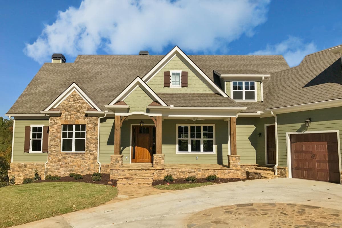 House plan exterior with stone accents, a covered front porch with wooden posts, multiple gables, and a side-entry garage.
