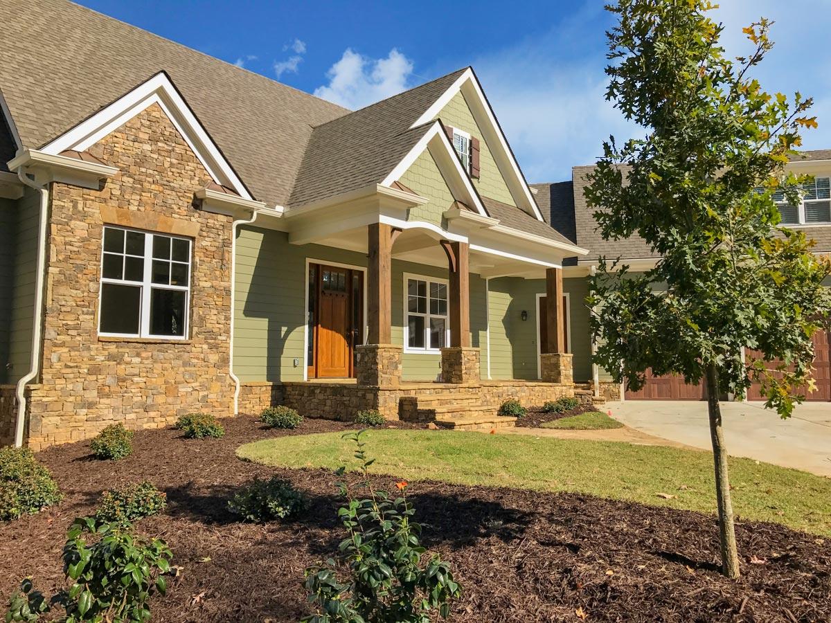Craftsman-style house plan exterior with stone accents, covered front porch with wooden posts, and a prominent gable.