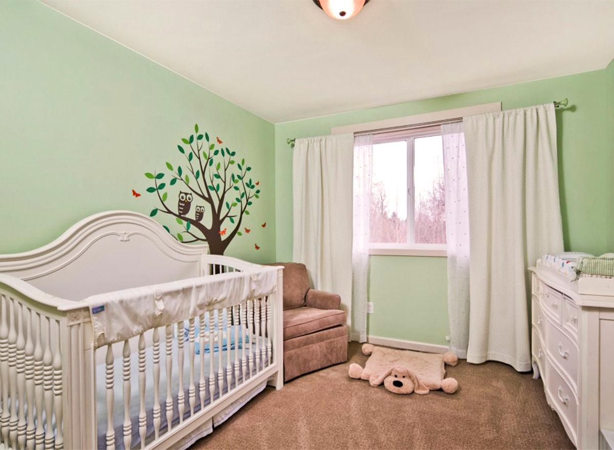 Nursery with white crib, armchair, dresser, and wall decal of a tree with owls.