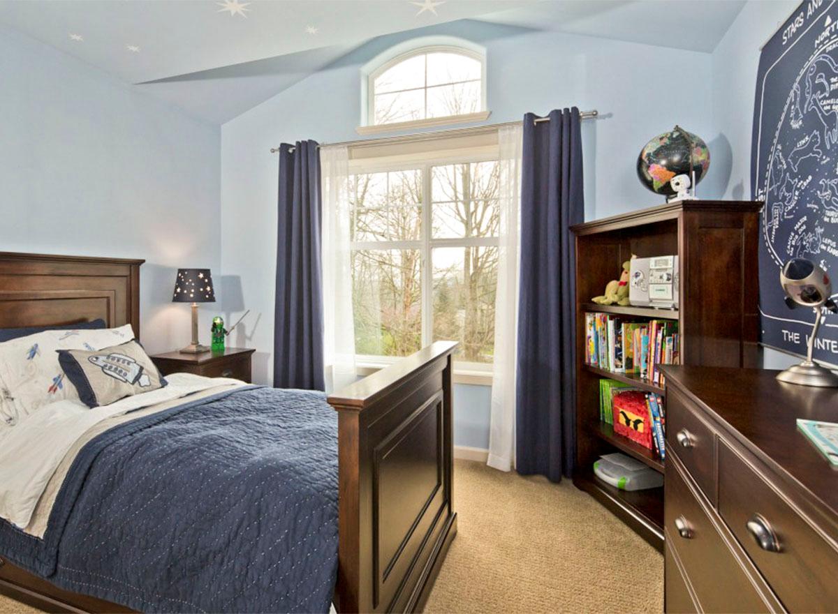 Children's bedroom with vaulted ceiling, arched window, bed, dresser, and bookshelf.